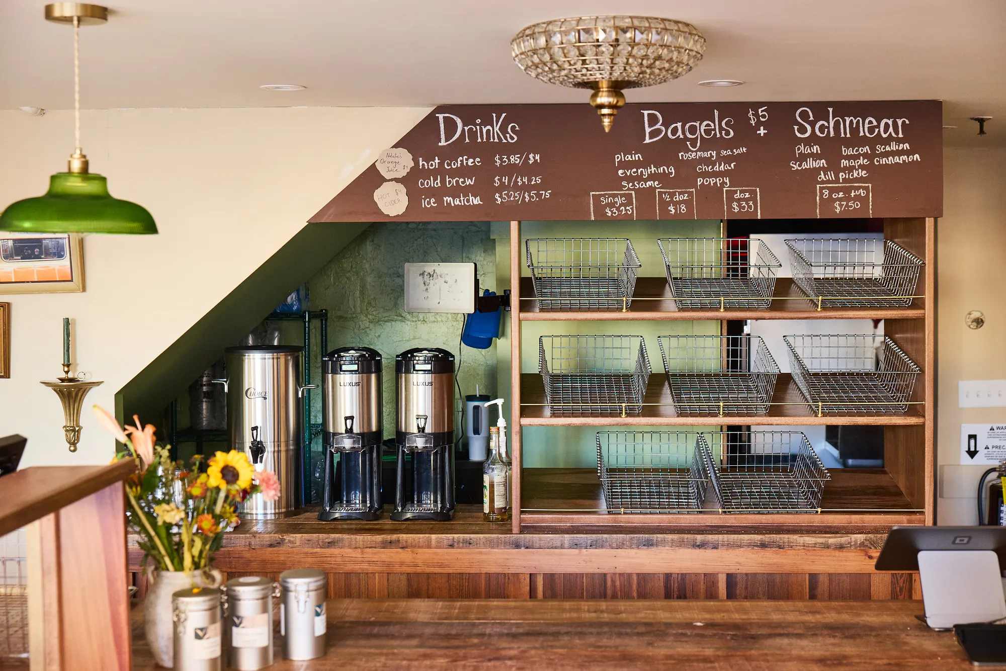 The menu wall at Brick Street Bagels, a chalk board over wire baskets and coffee urns