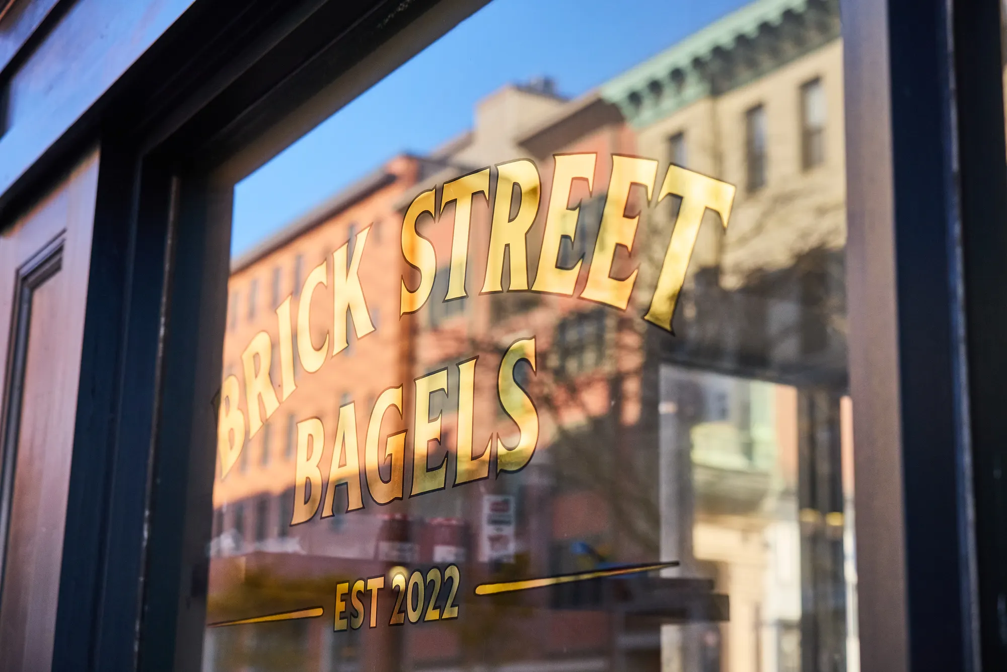 The gold-leaf sign on the window, with the brick buildings across the street reflected in the glass.
