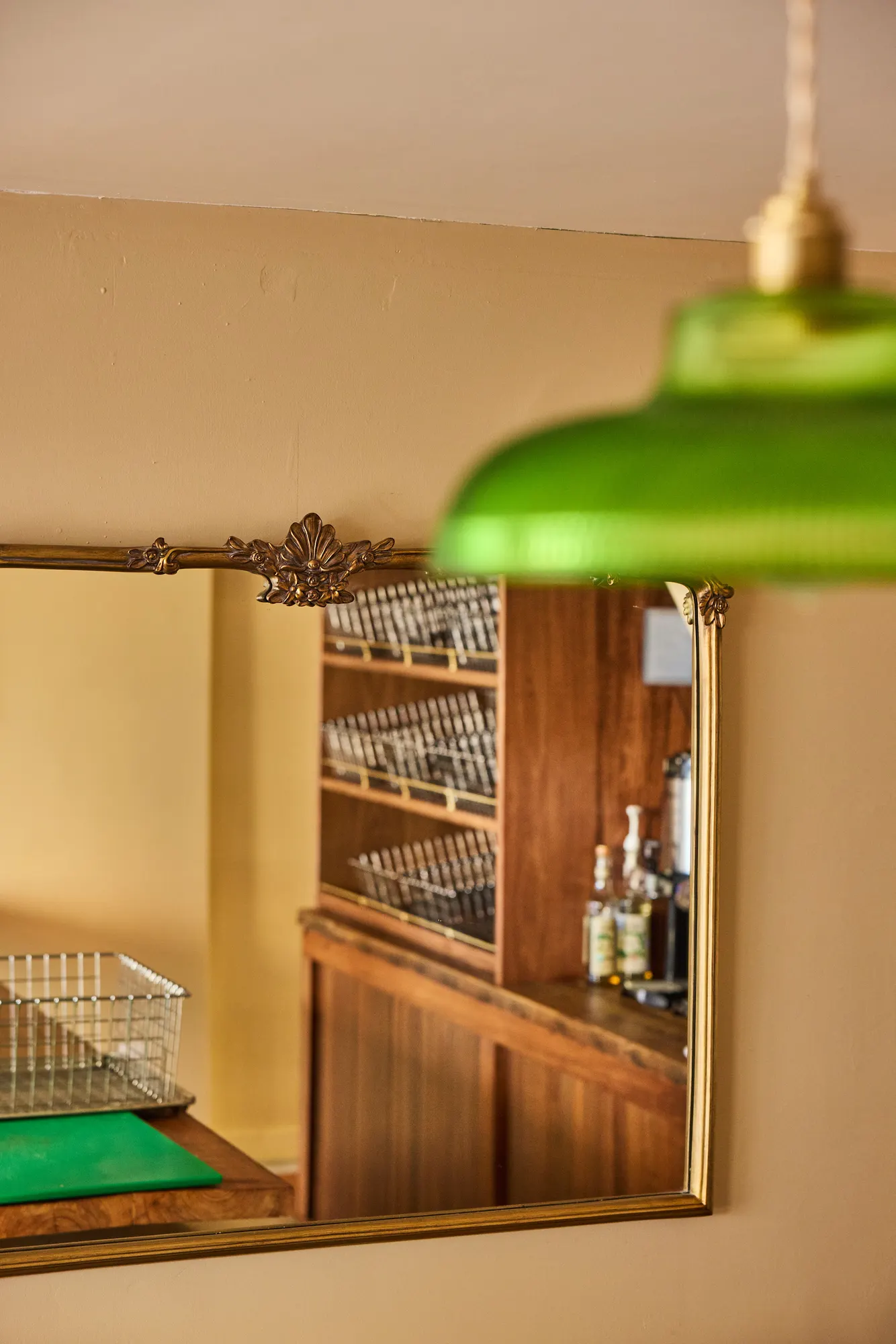 A gilt-framed mirror reflecting the baskets and shelving, under a green glass pendant.