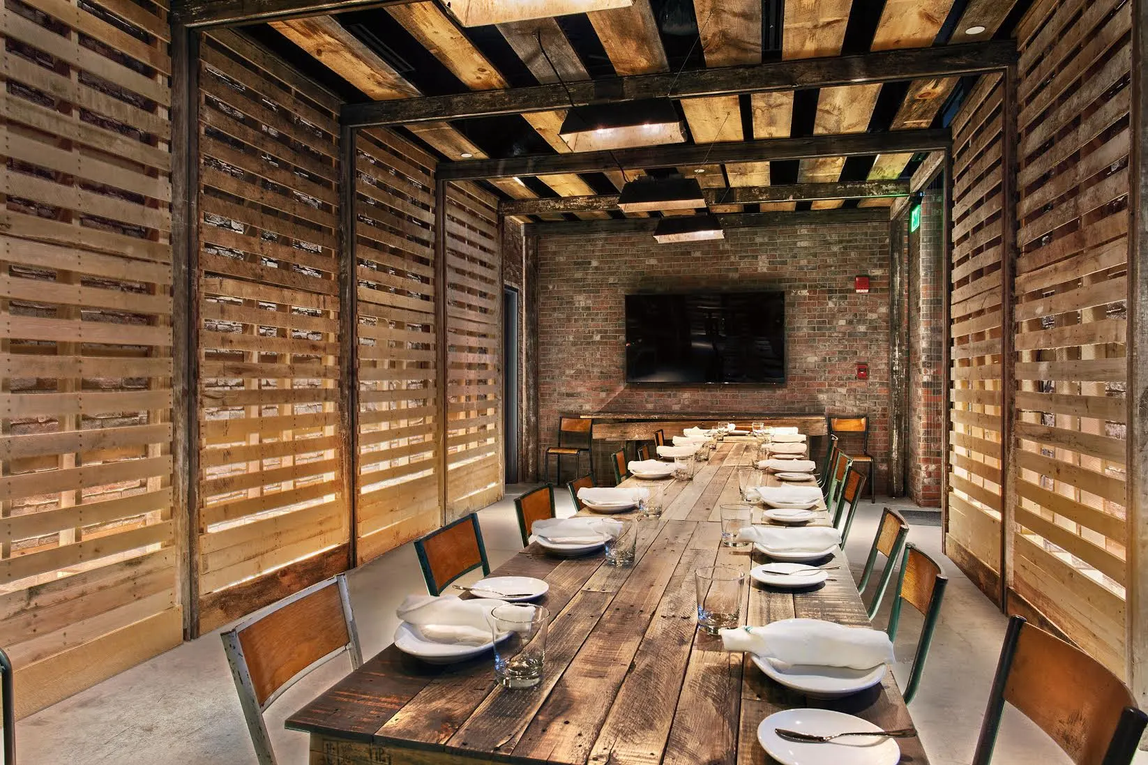 A long table set for dinner in a room walled with reclaimed timber slats.