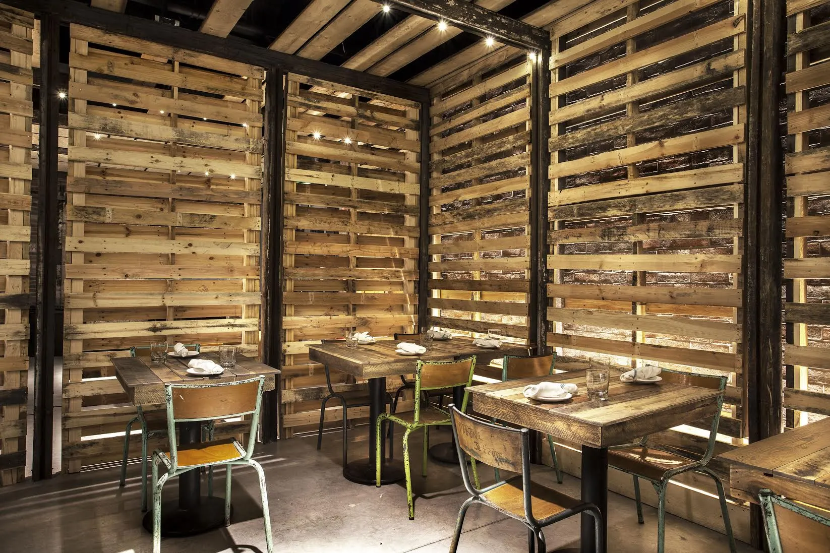 Timber tables and metal chairs inside walls of reclaimed timber slats.