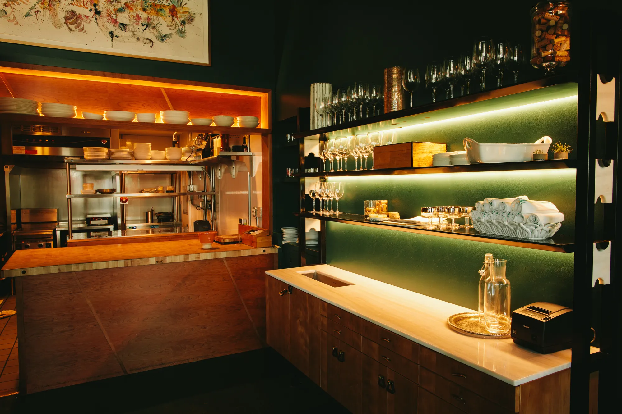 Backlit shelving carried over the counter, with the kitchen open behind it.