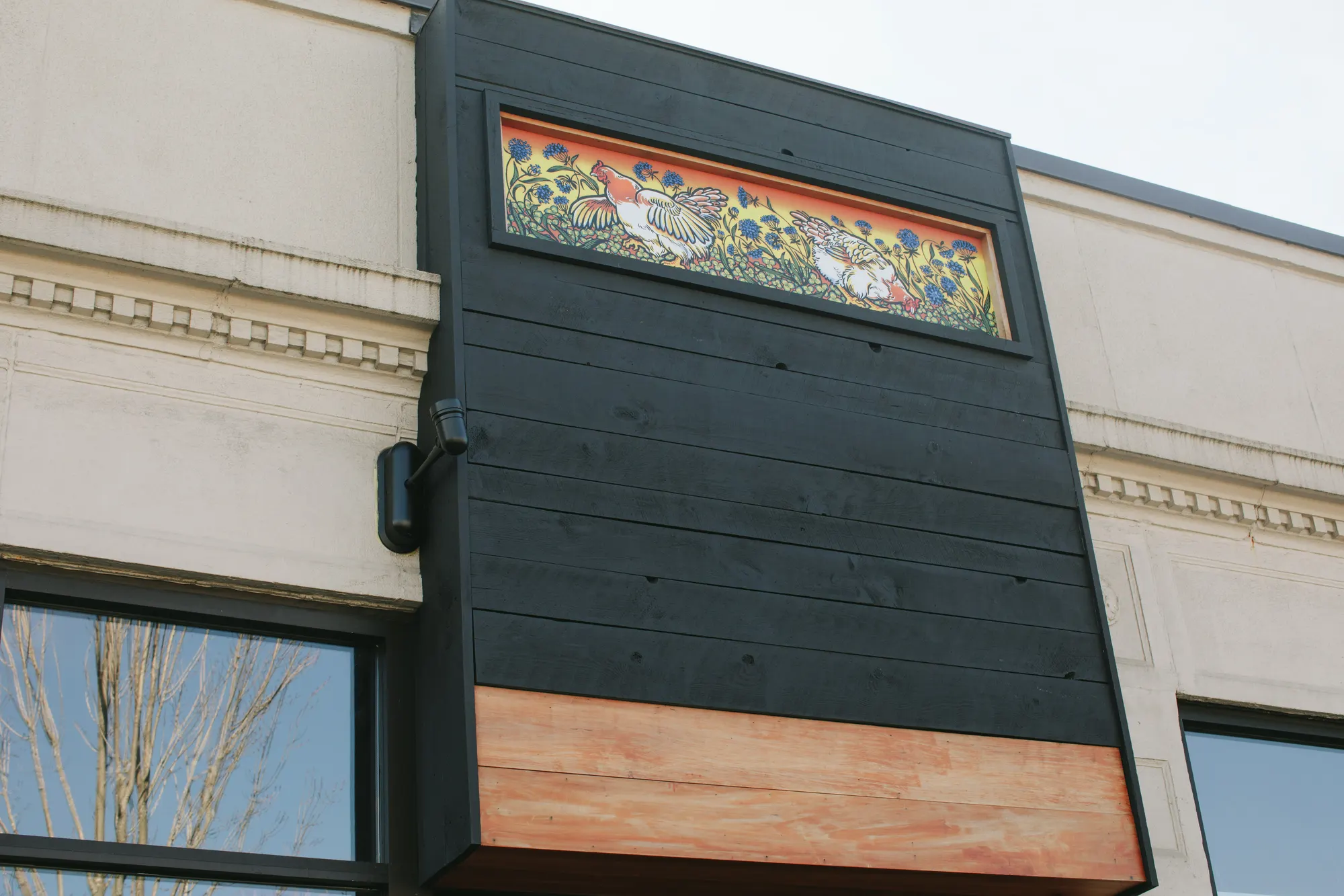 A dark clad box pushed out over the street, with a painted panel set into its face.