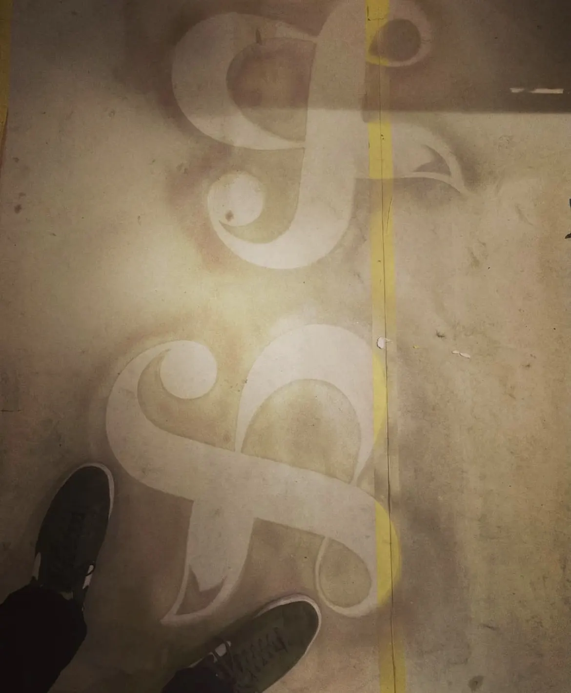 The restaurant's monogram projected in light on the concrete floor, a pair of sneakers at the edge of the frame.