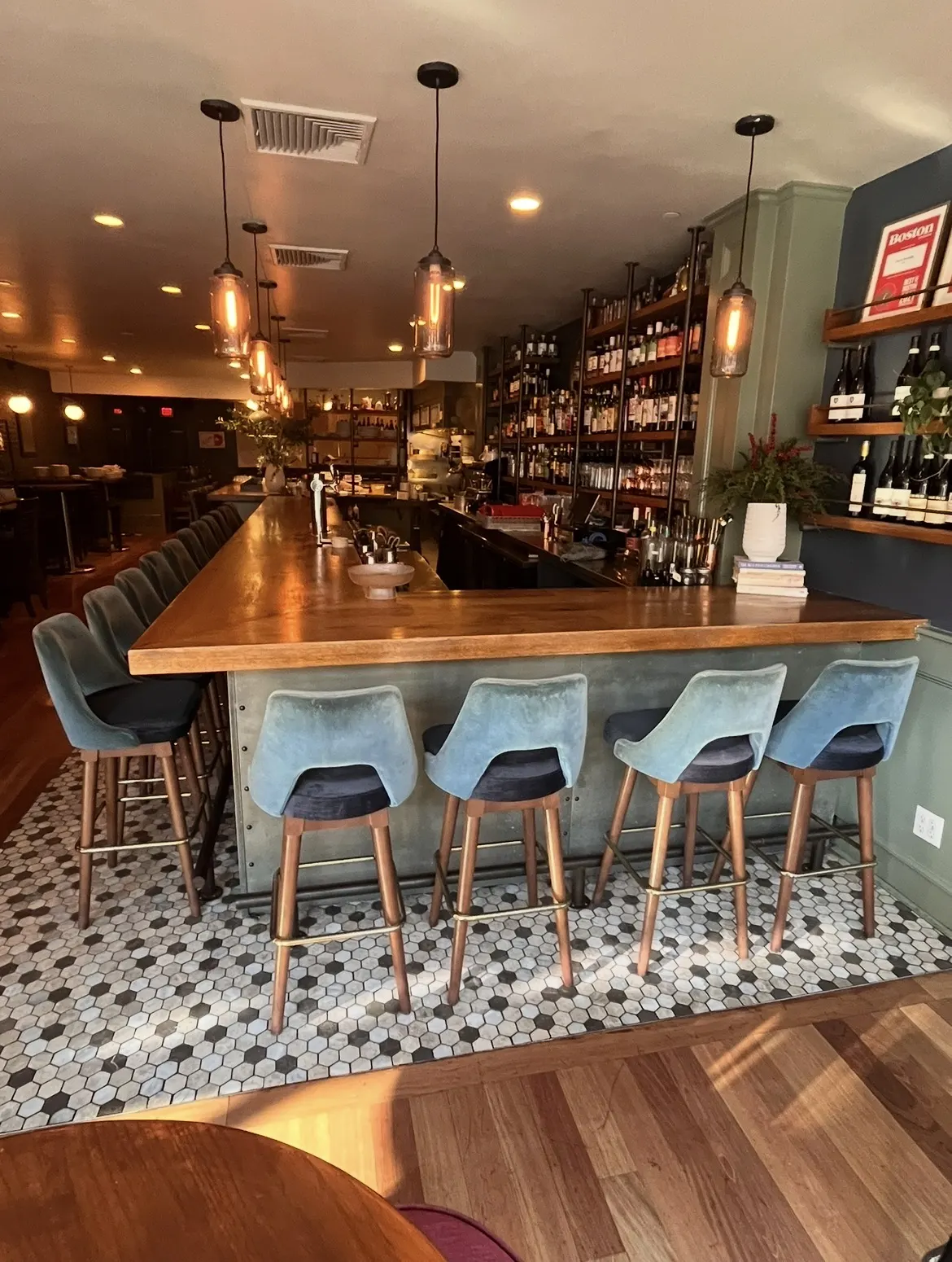 The bar at Fox & the Knife, blue velvet stools along a timber-topped bar on hexagonal tile
