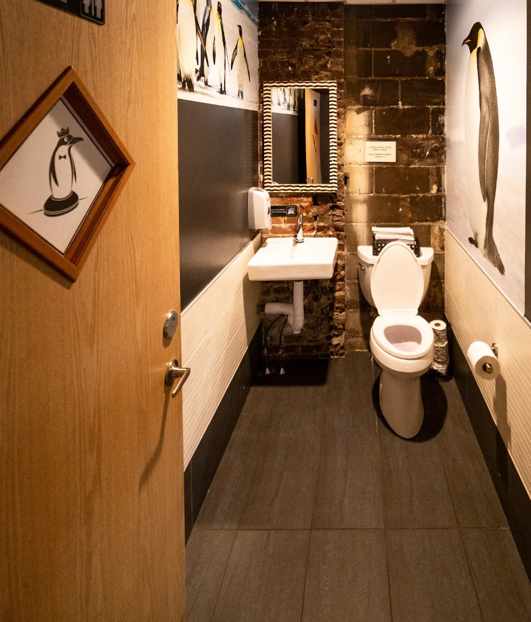 A restroom with penguin artwork and a mirror over the basin.