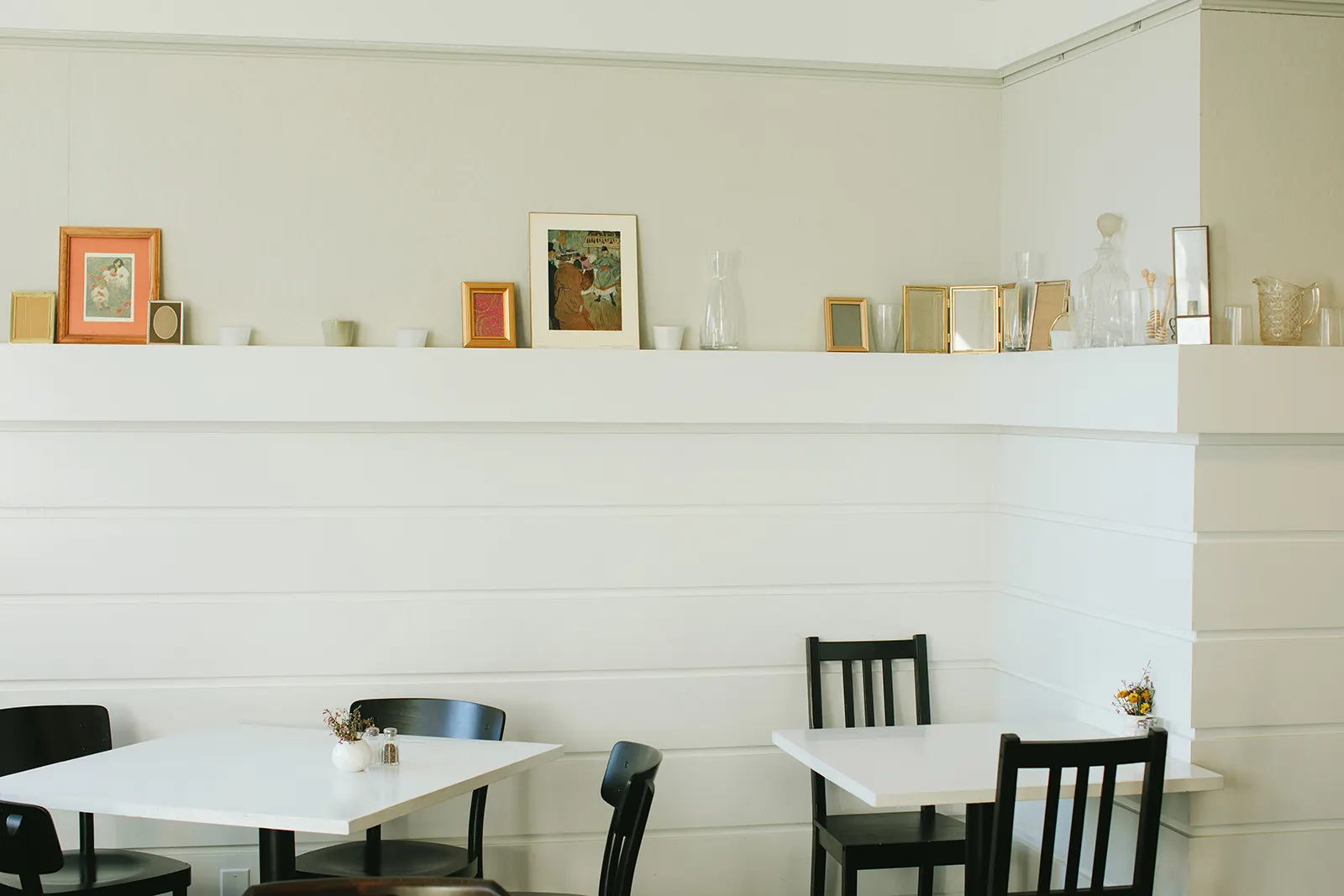Juliet: white tables and black chairs below a ledge of framed prints on white panelling