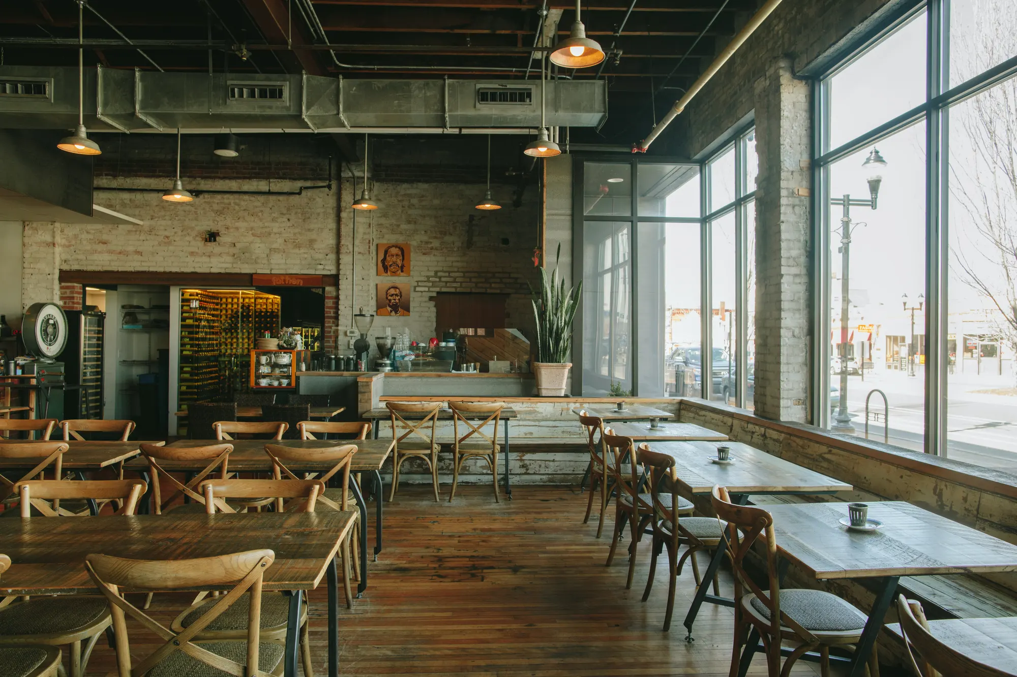 Rows of timber tables and cross-back chairs along the tall street windows, under exposed ductwork.