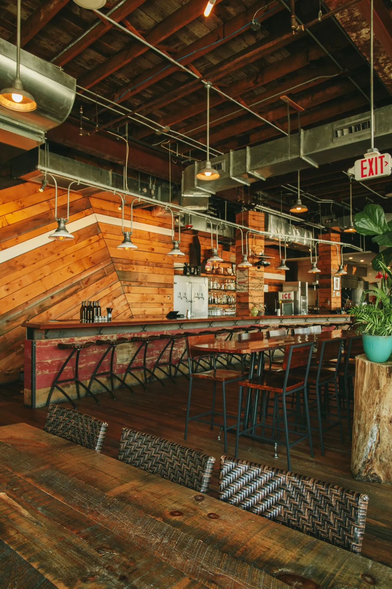 The long bar under diagonal timber cladding, with a woven banquette and high tables in front of it.