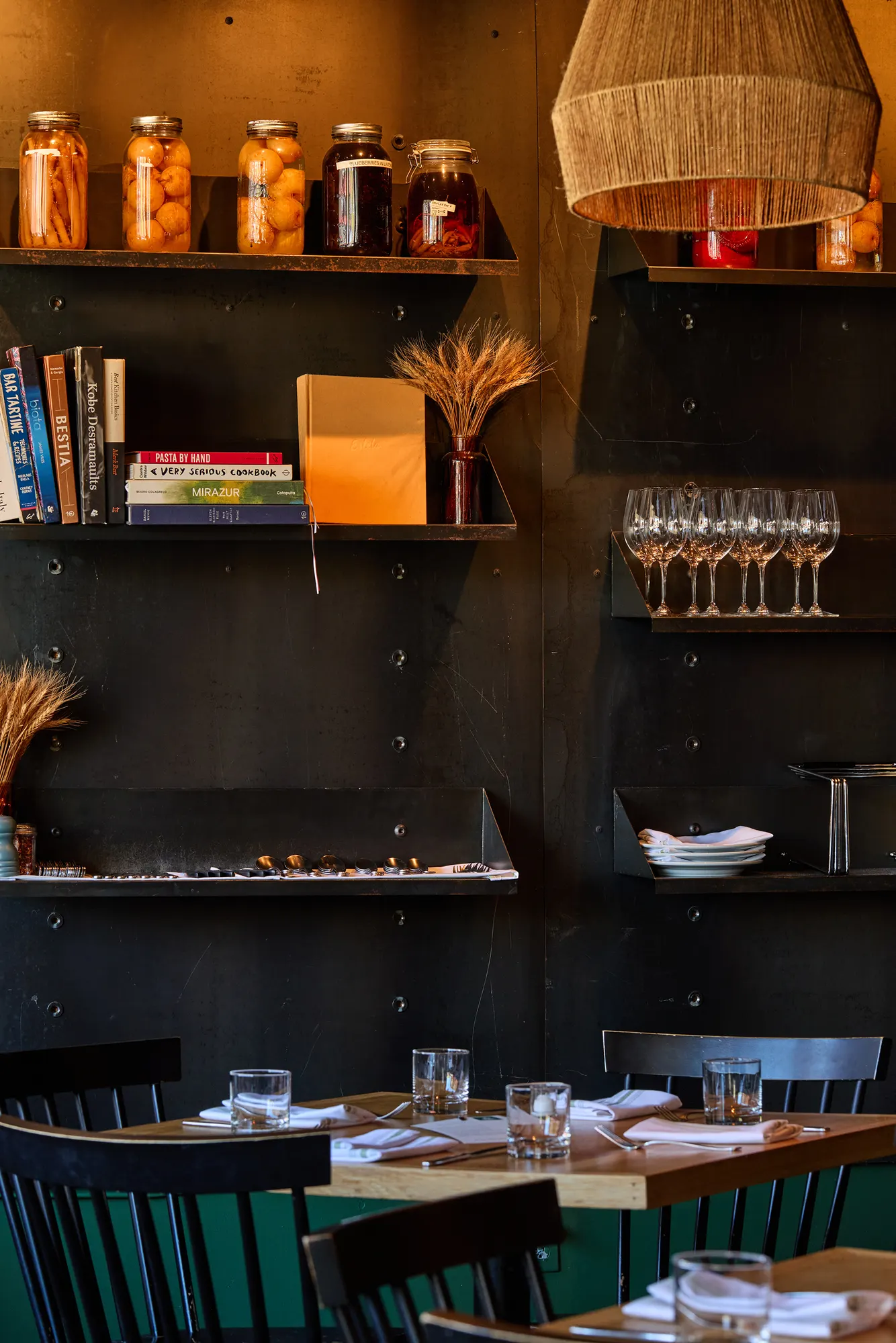 Jars, cookbooks and glasses on steel shelves above a set table.