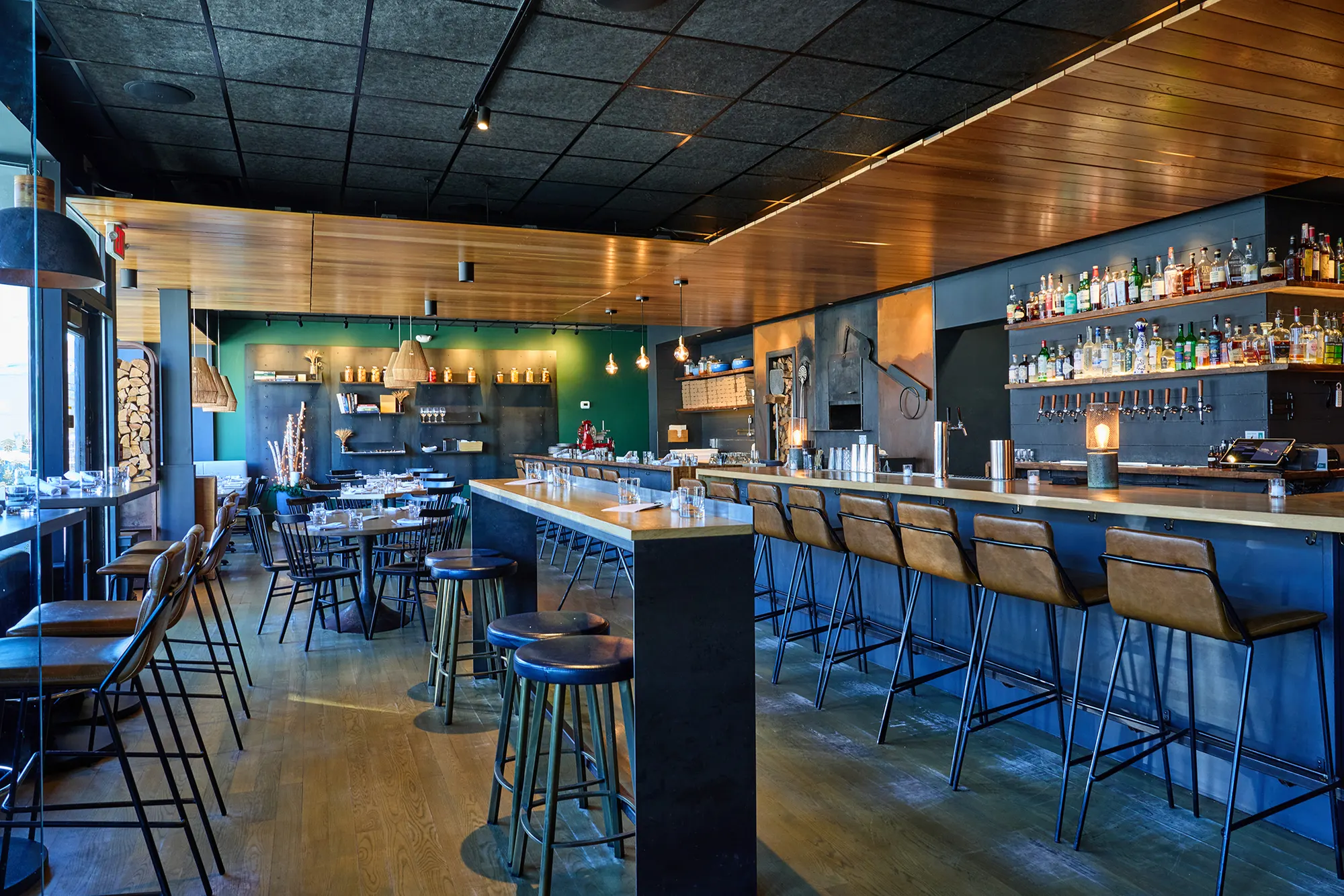 The bar and dining room at Prairie Fire, leather stools along a blue bar under a timber ceiling