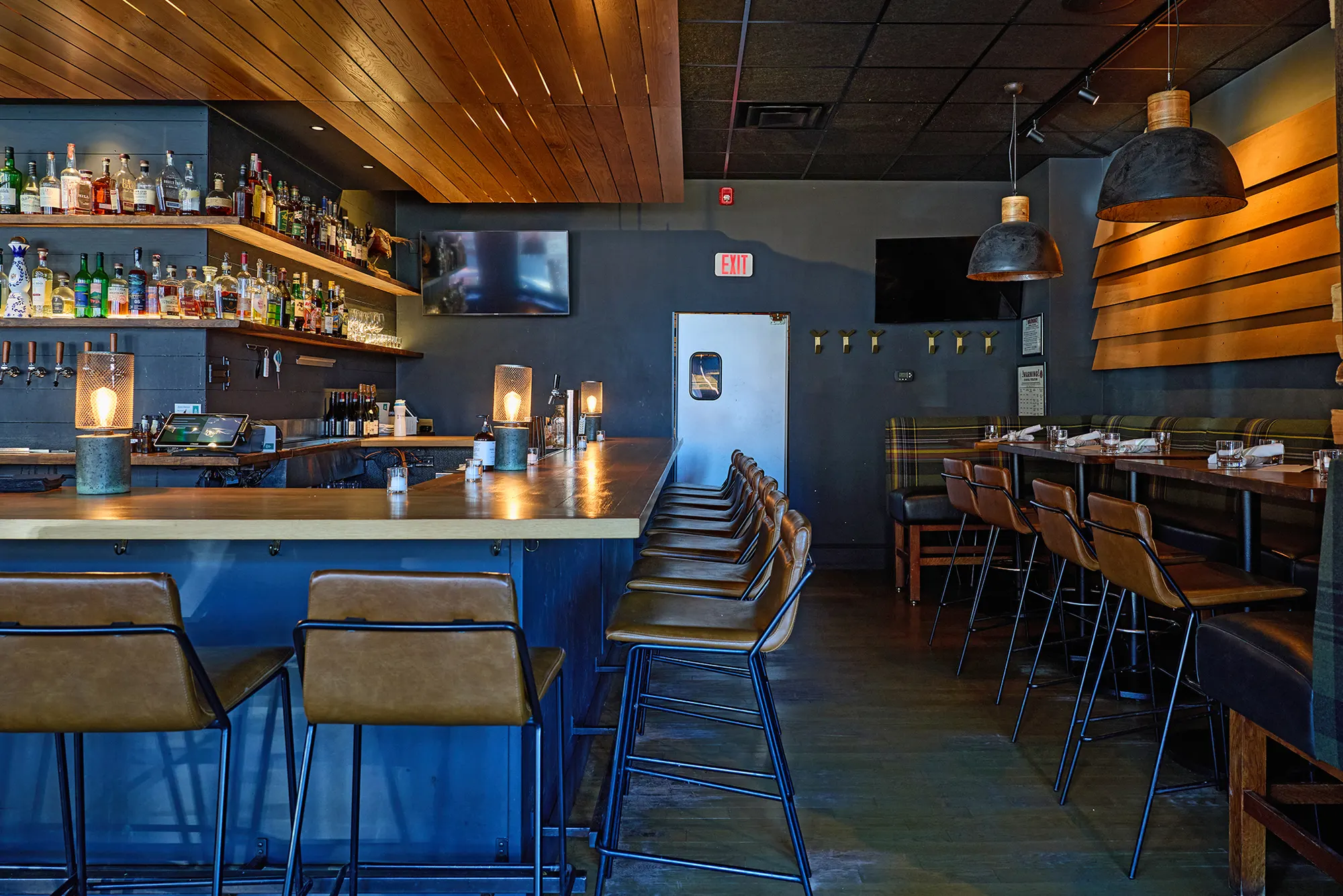 The bar and its stools running toward the back, under dome pendants.