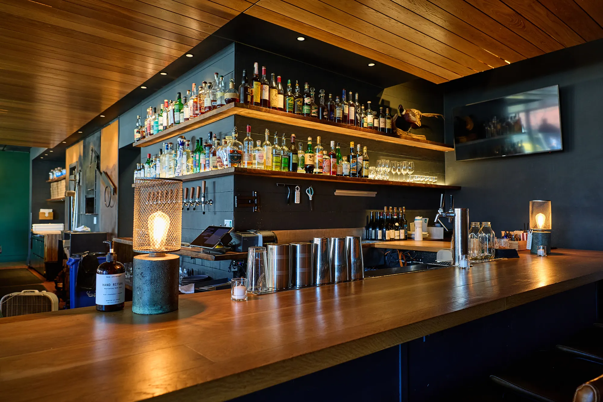 The bar top and back bar, lit by a lantern and a hanging bulb.