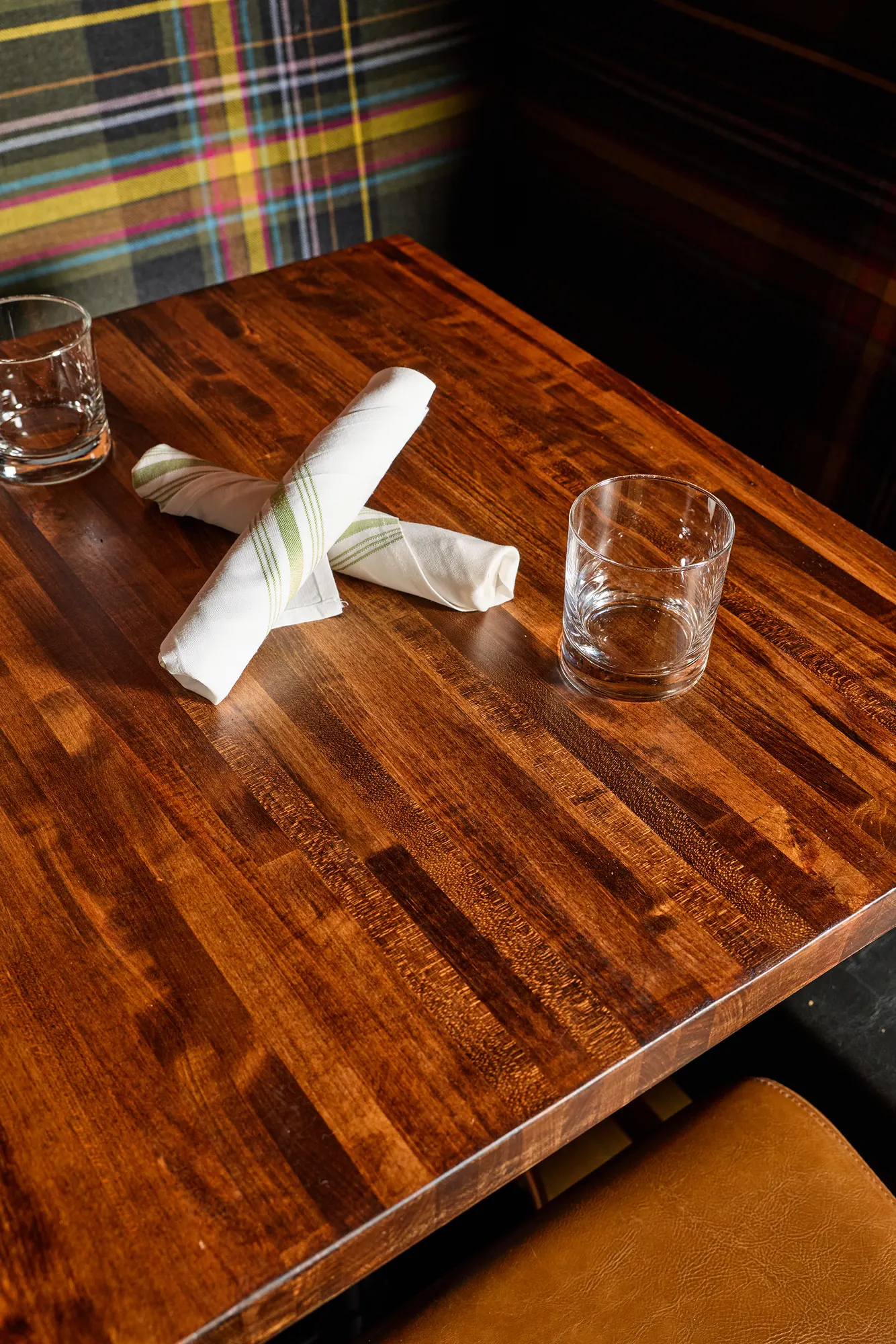 A butcher-block table set with napkins and glasses against the plaid banquette.