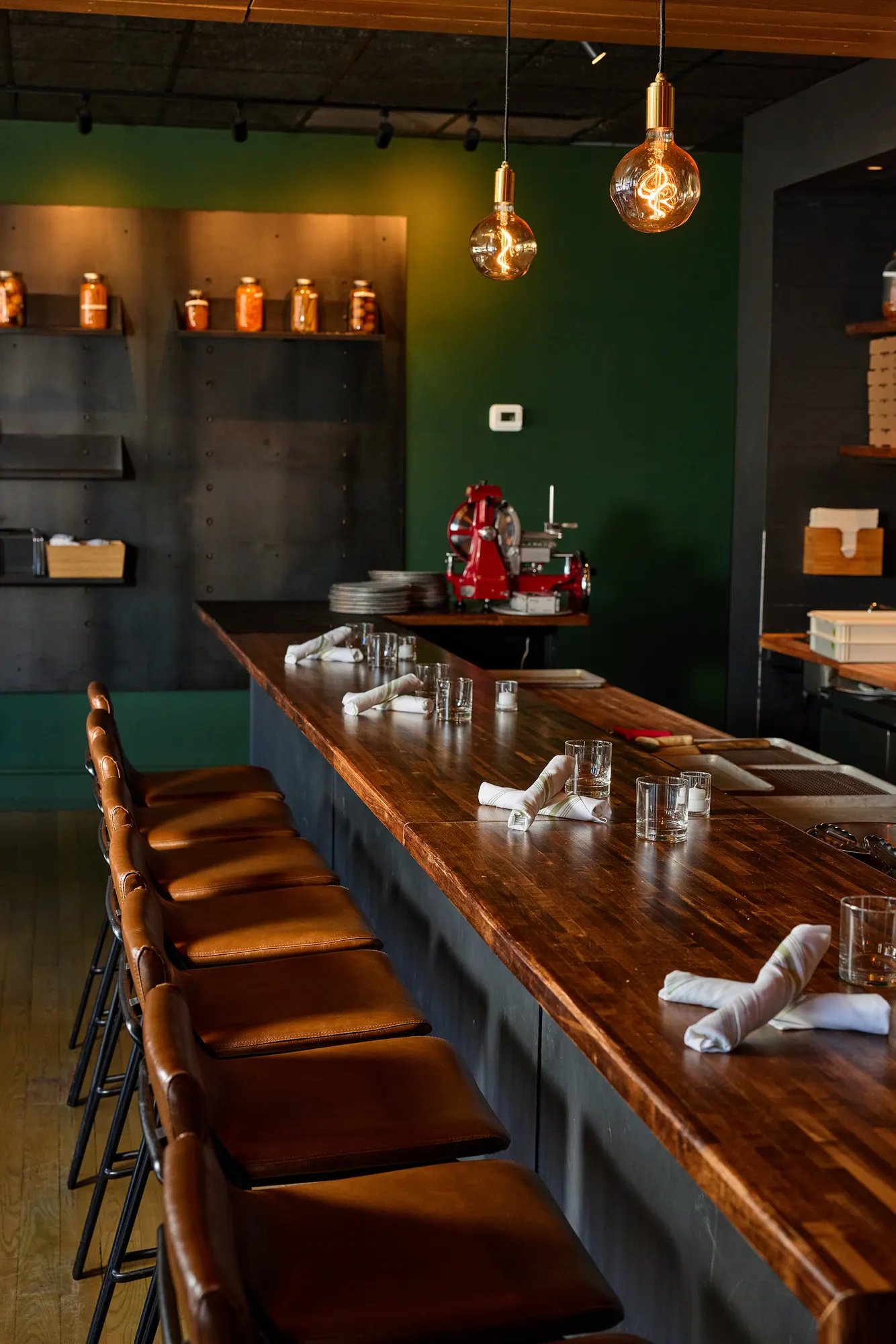 Leather stools along the walnut counter, under globe bulbs and the green wall.