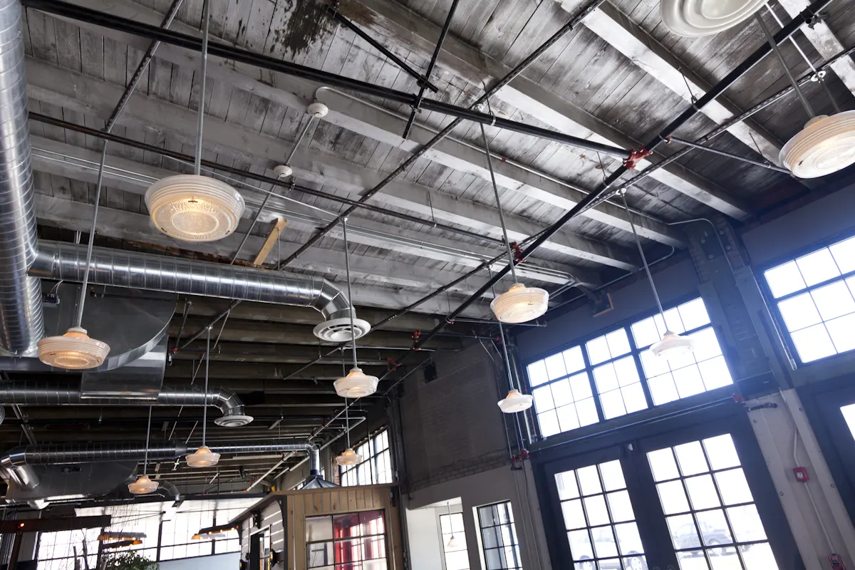 Lights hung among the ductwork, with the steel windows beyond.