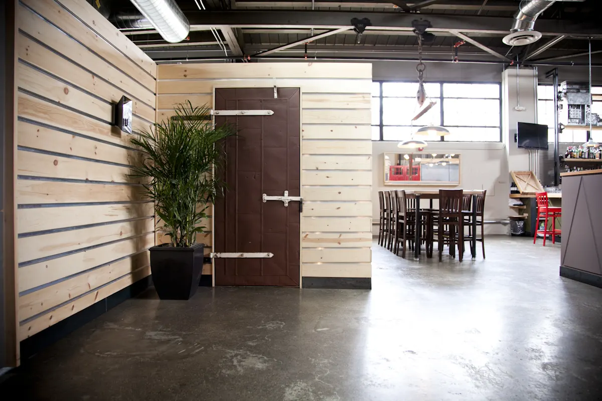 A heavy door on strap hinges in a timber-clad wall, the dining room beyond.