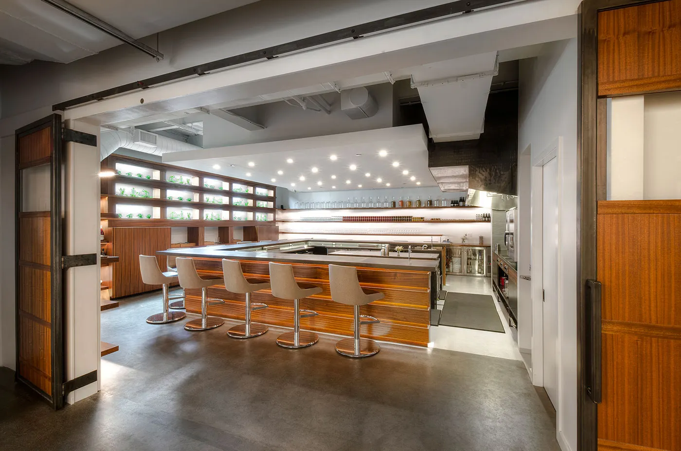 The room seen past an open timber and steel door, upholstered stools along a timber-clad counter.