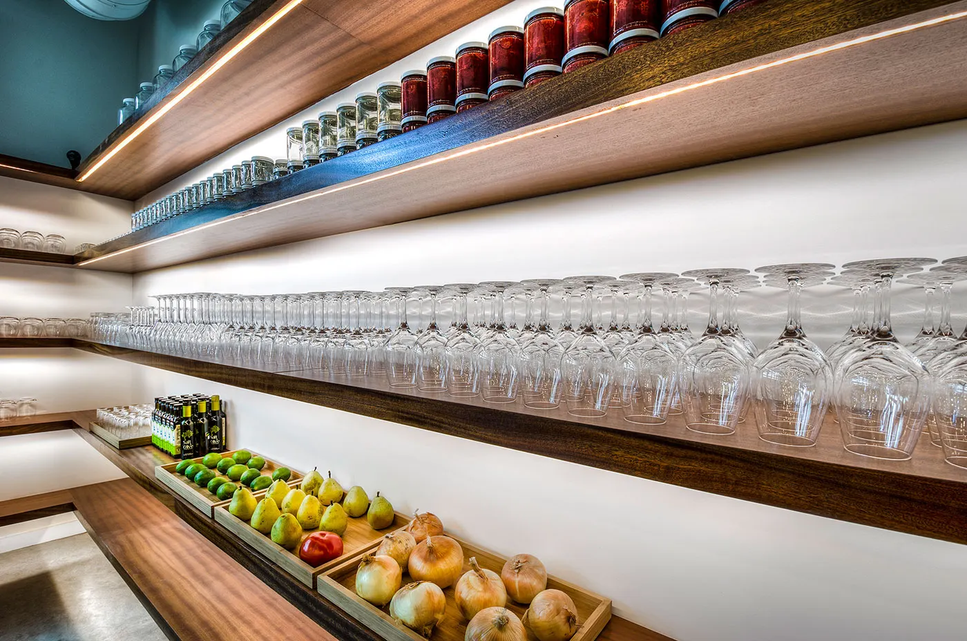 A long shelf of glasses above a line of fruit.