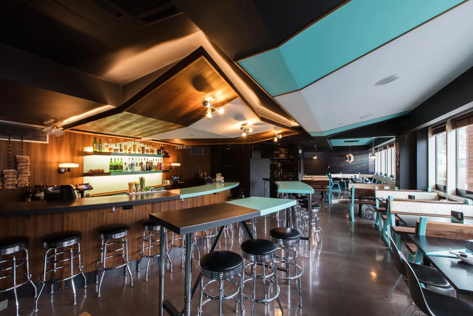 Chrome stools at a teal-topped counter, with the lit back bar beyond.