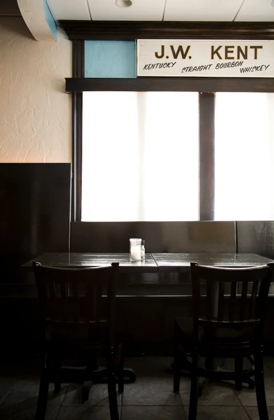 A table by a window under a J.W. Kent whiskey sign.