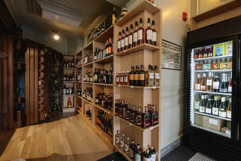 Timber shelves of spirits and a glass-fronted refrigerator in a small side room.