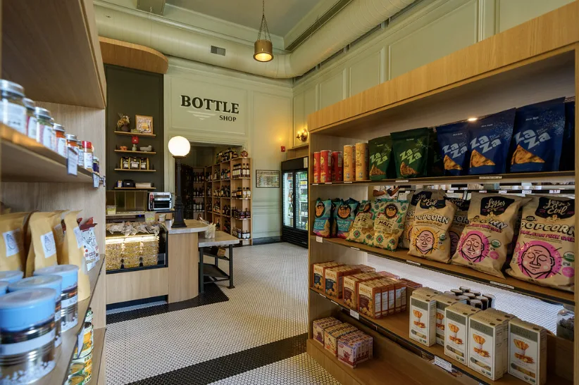 Shelves of snacks and pantry goods leading to a doorway signed BOTTLE SHOP.