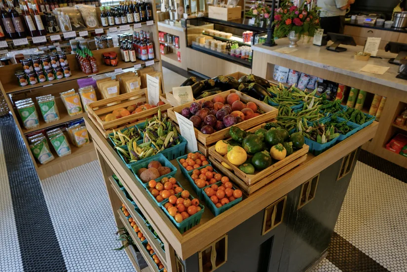 Crates of fruit and vegetables on a timber display, with grocery shelves and the counter behind.