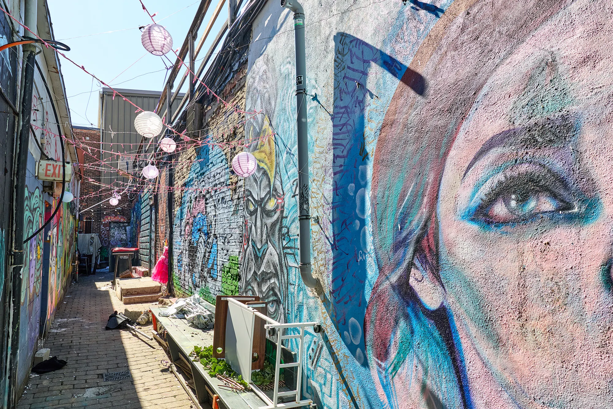 A large painted face along the alley wall, with lanterns overhead.