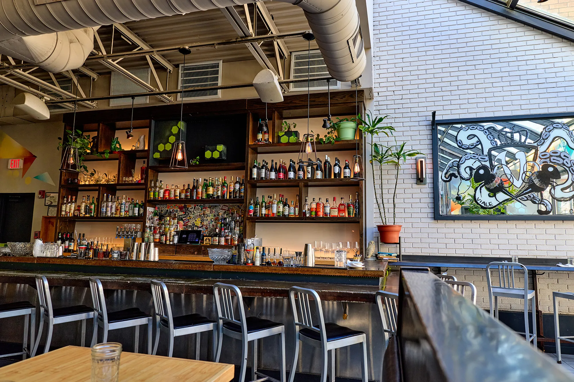 A wall of bottle shelves behind the bar, beside a framed artwork on white brick.