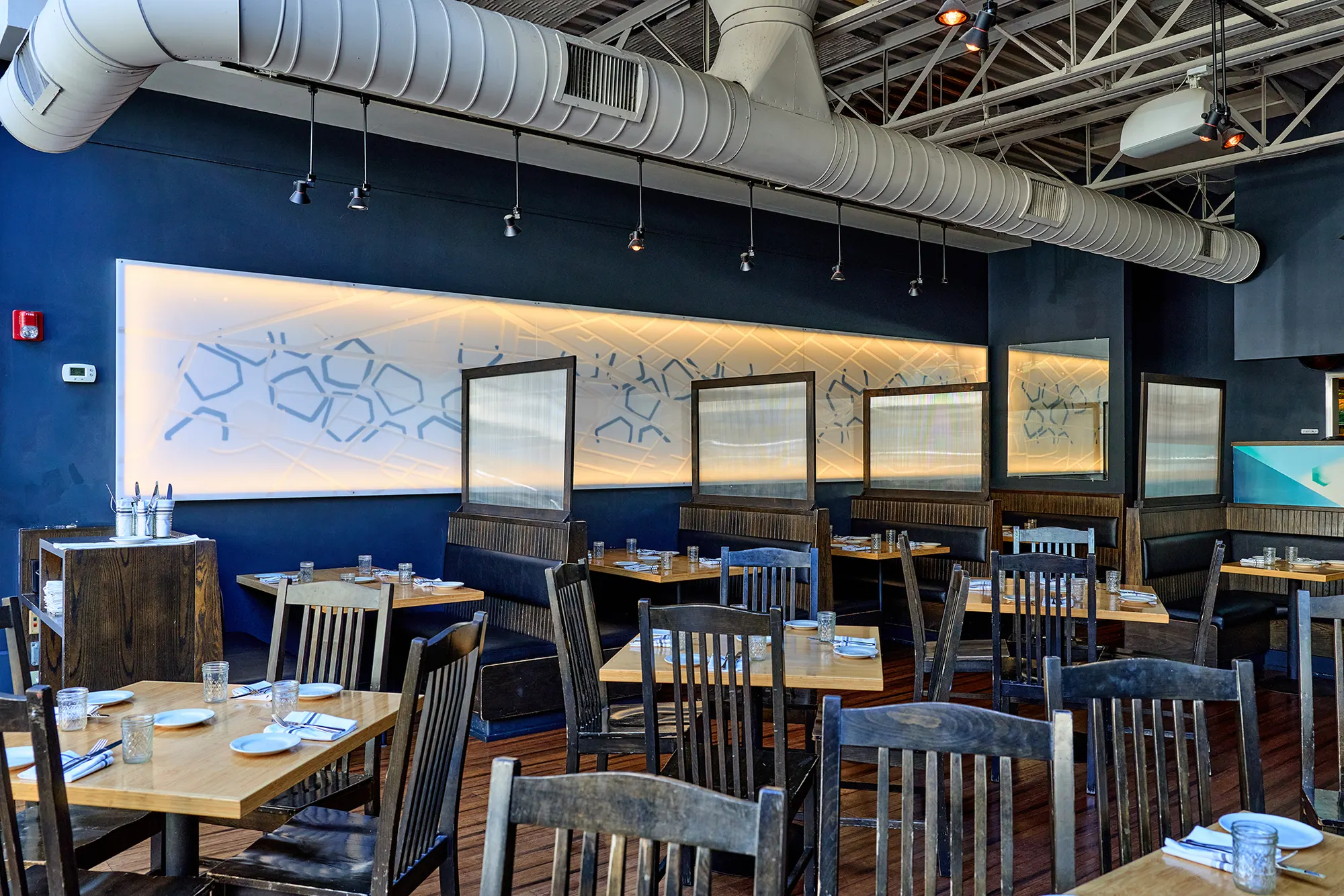 Tables and dark chairs beneath a backlit wall of honeycomb patterns.