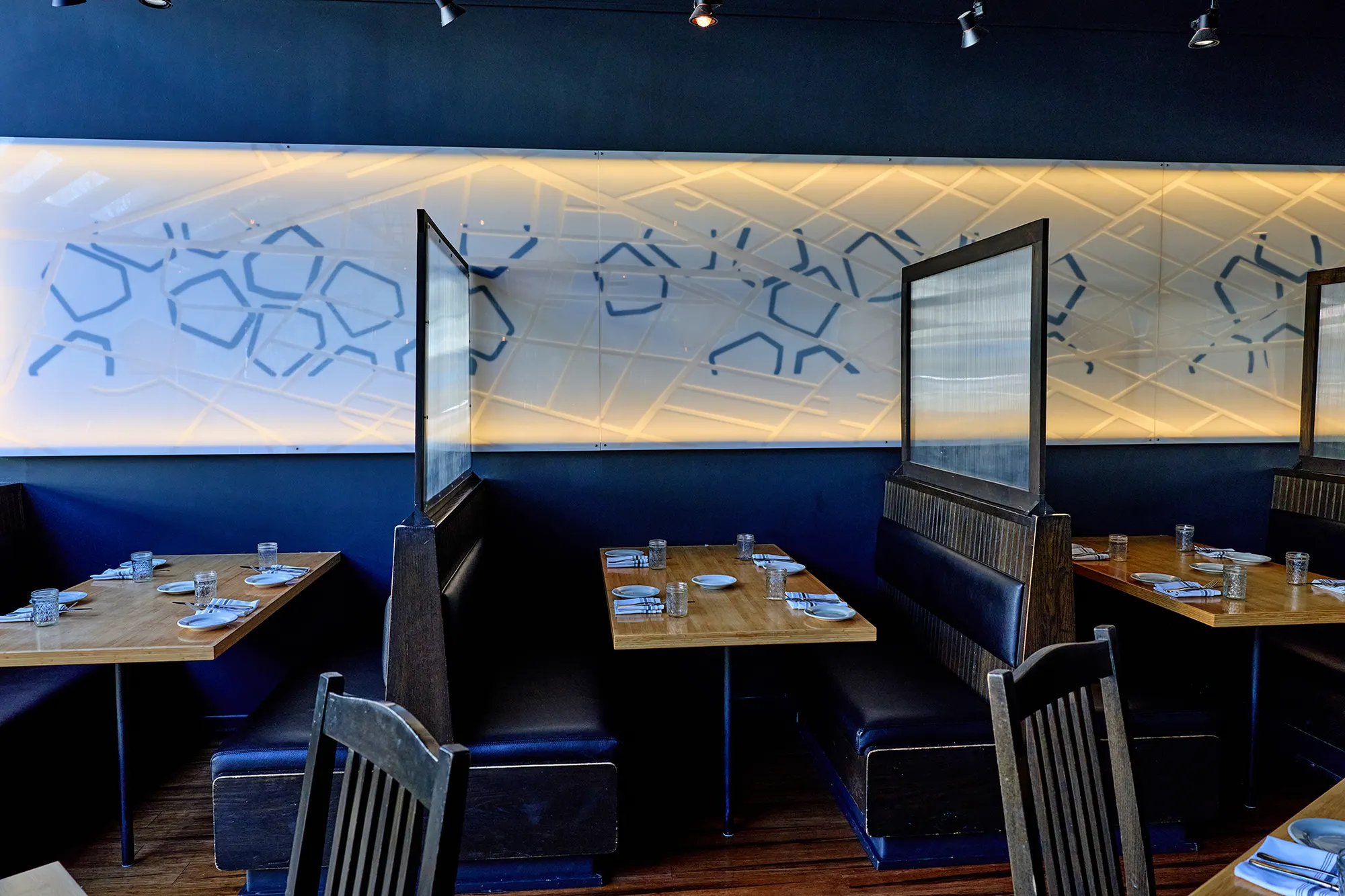 Tables below the backlit honeycomb wall, with frosted screens between the booths.