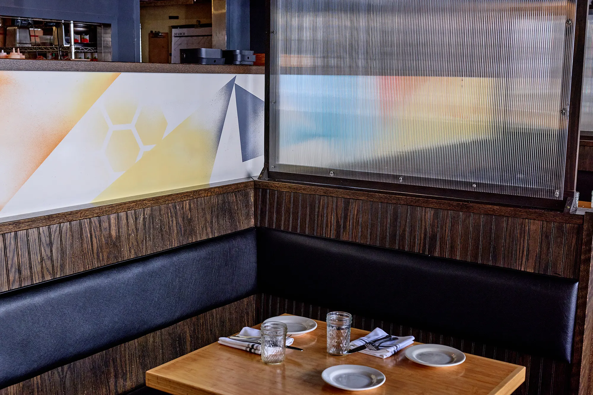 Two booth tables at the corner of the banquette, with a frosted screen above.