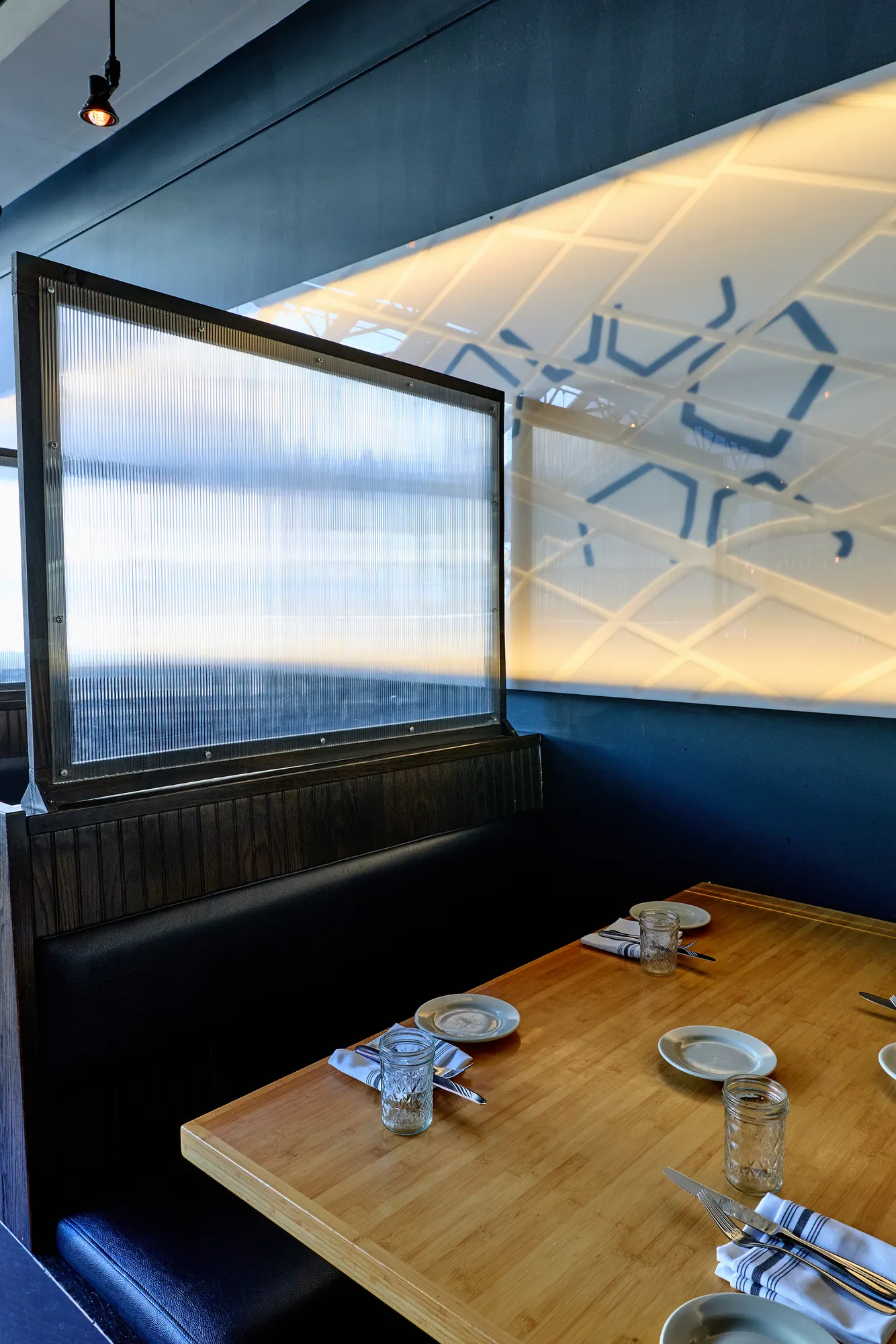 A booth table beside a frosted screen and the backlit wall.