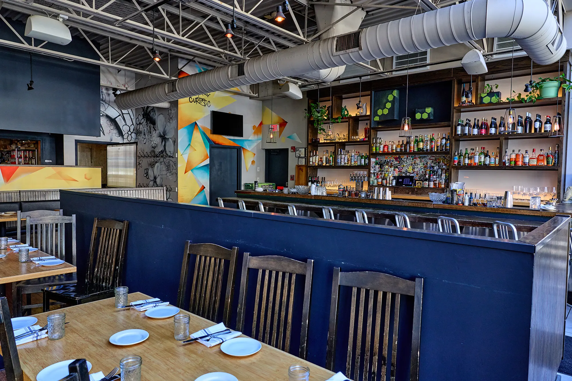 Dark chairs along the banquette, with the bar and painted panels beyond.