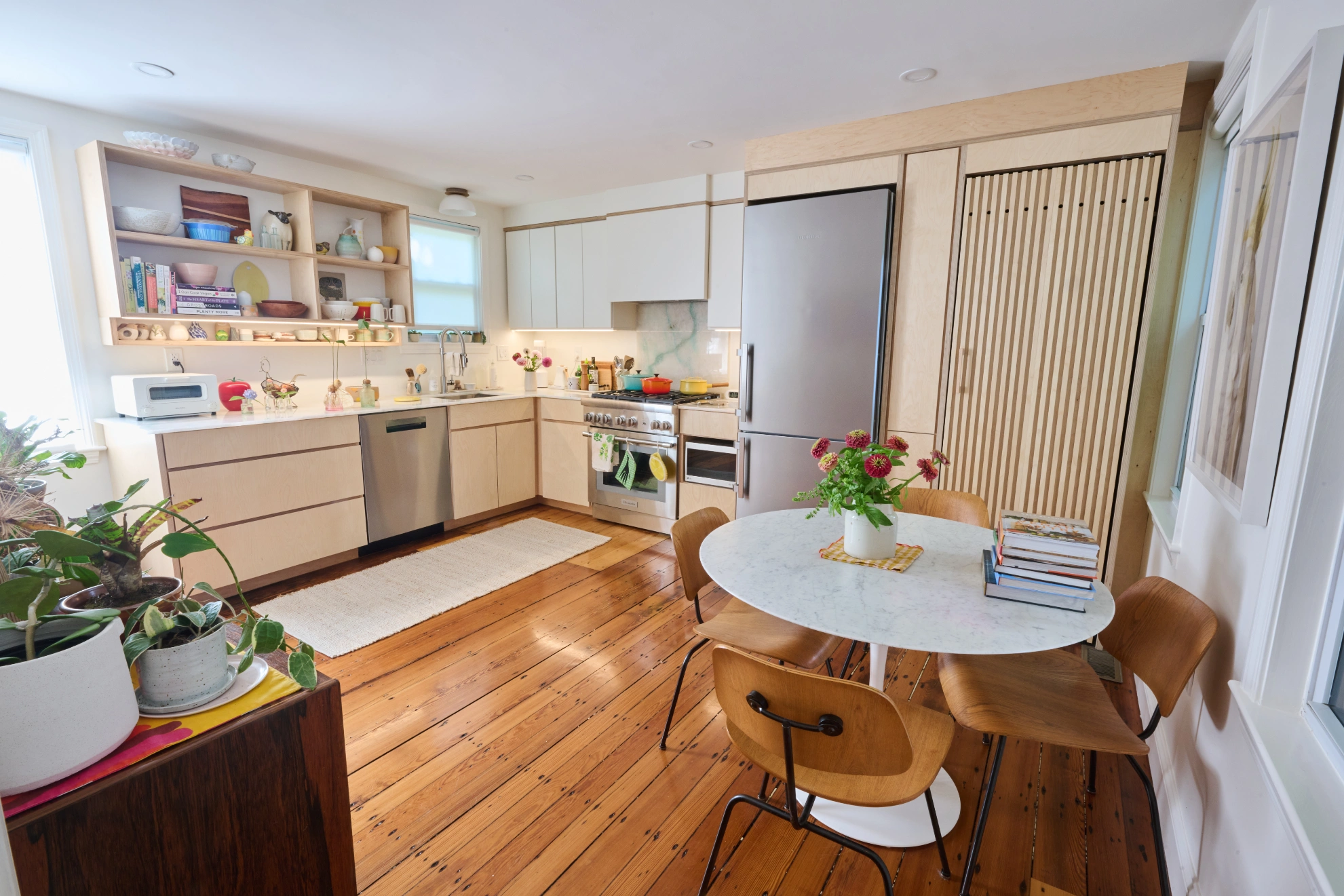 The kitchen and dining room at Chalk, birch cabinets and open shelves around a round marble table