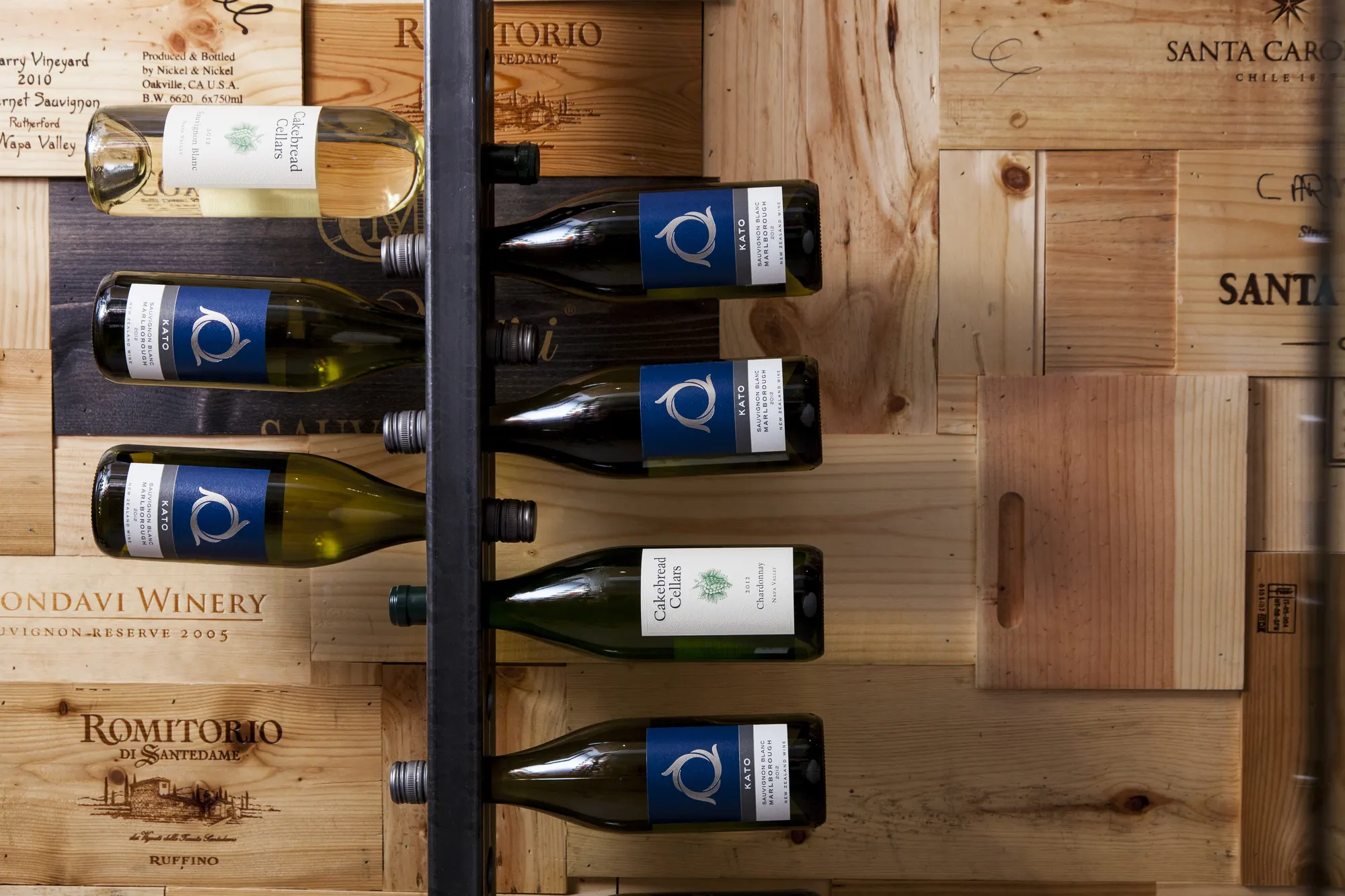 Bottles held on steel rods against stamped wine-crate boards.