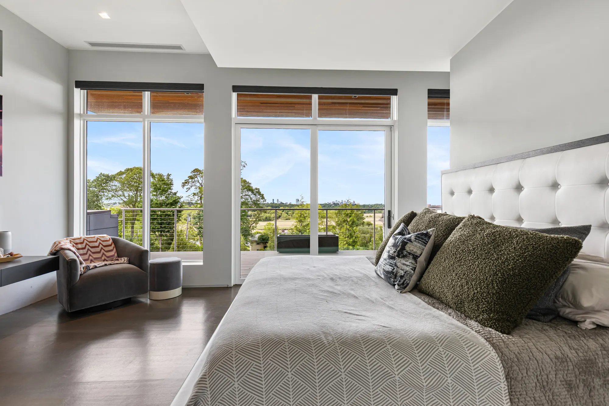 The bed and an armchair in front of a run of tall windows onto the deck.
