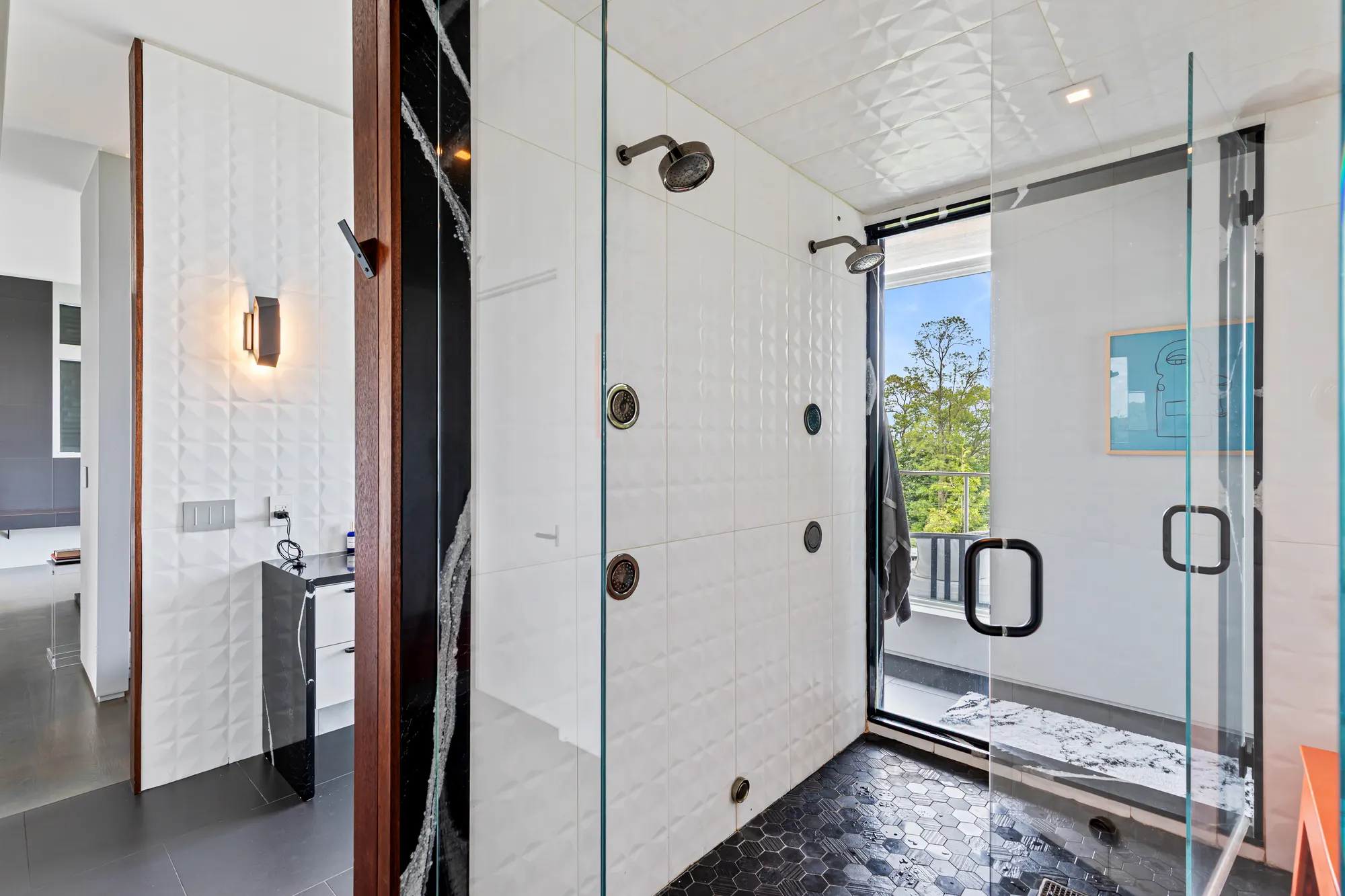 A glass-walled shower in white textured tile with a black hexagon floor, and a glass door to the deck.