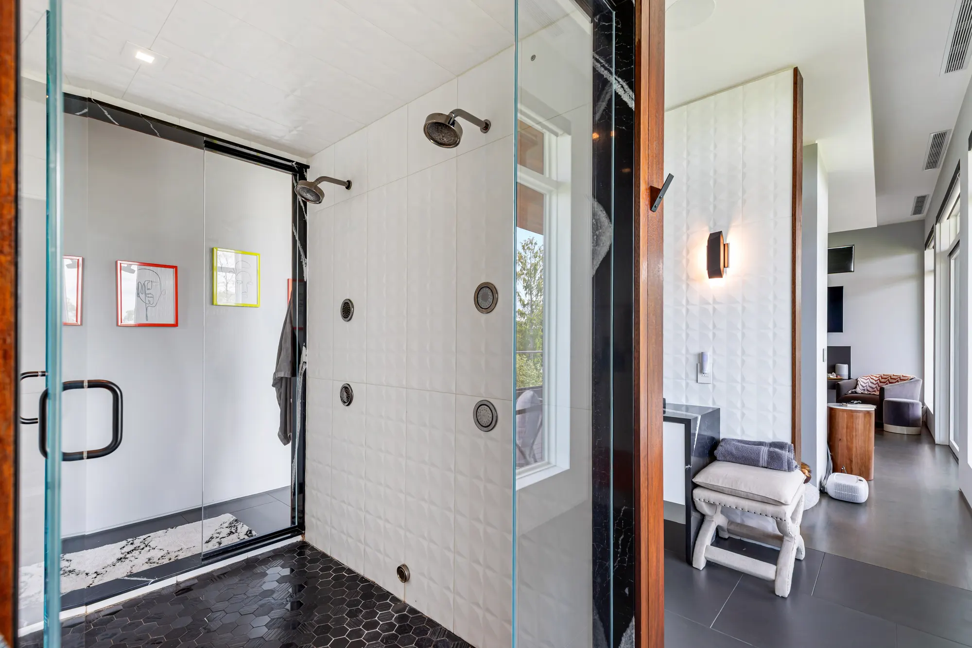 The glass shower in white tile and black hexagon floor, the vanity stool beyond.