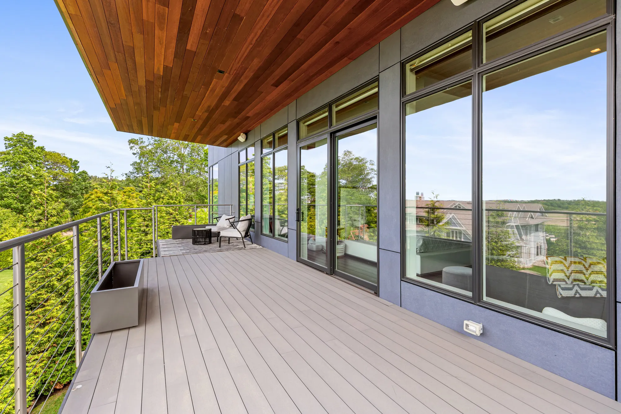 A long deck with a cable rail, under the timber soffit, beside the glass wall of the house.