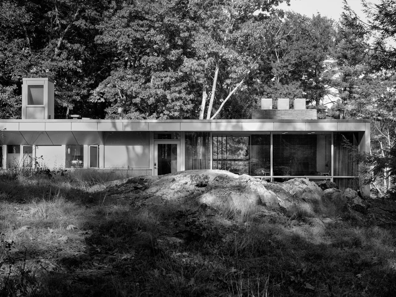 The single-storey front behind a rock outcrop, a run of glazing under the flat roof.