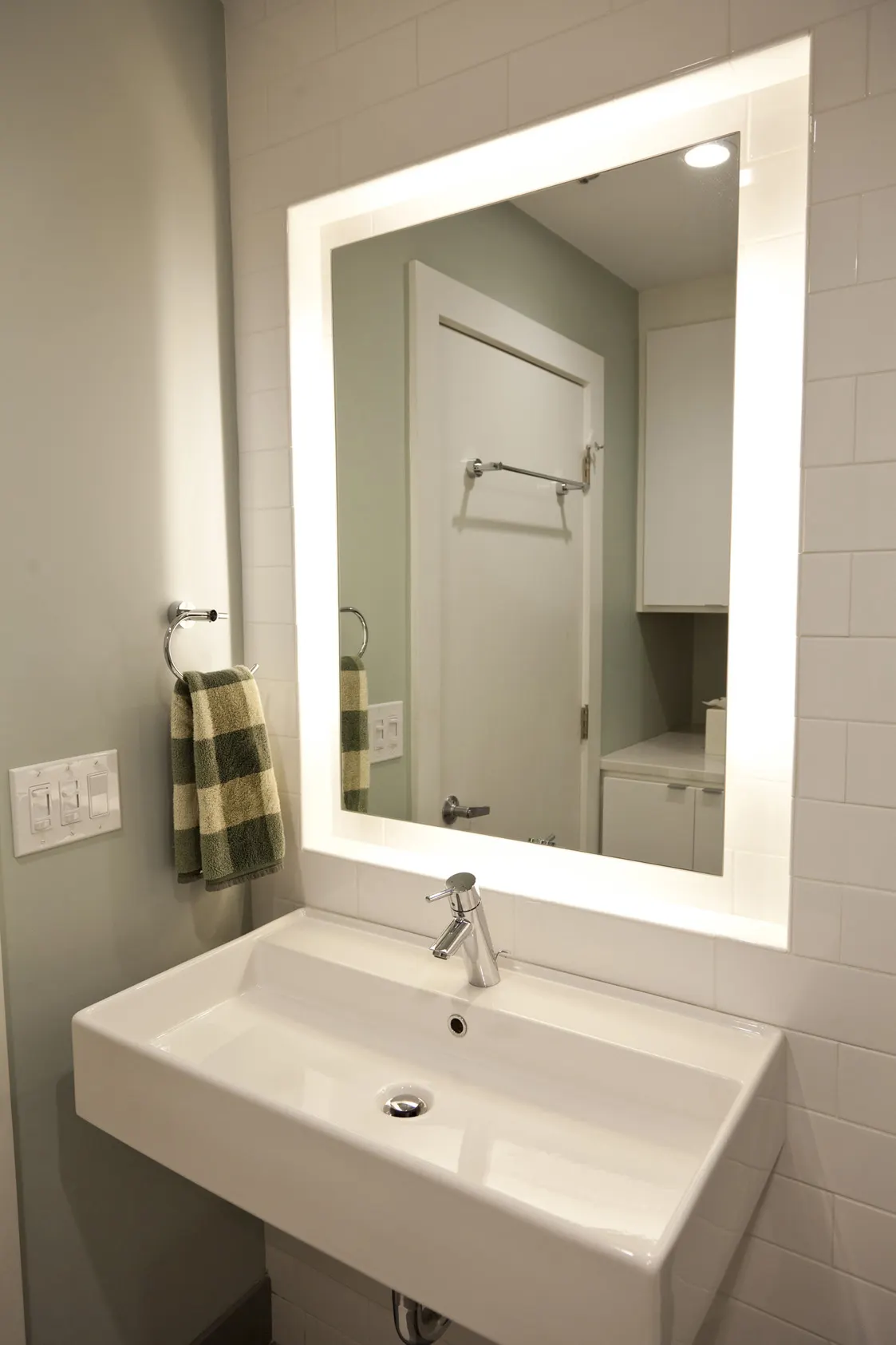 A wall-hung white basin under a backlit mirror.