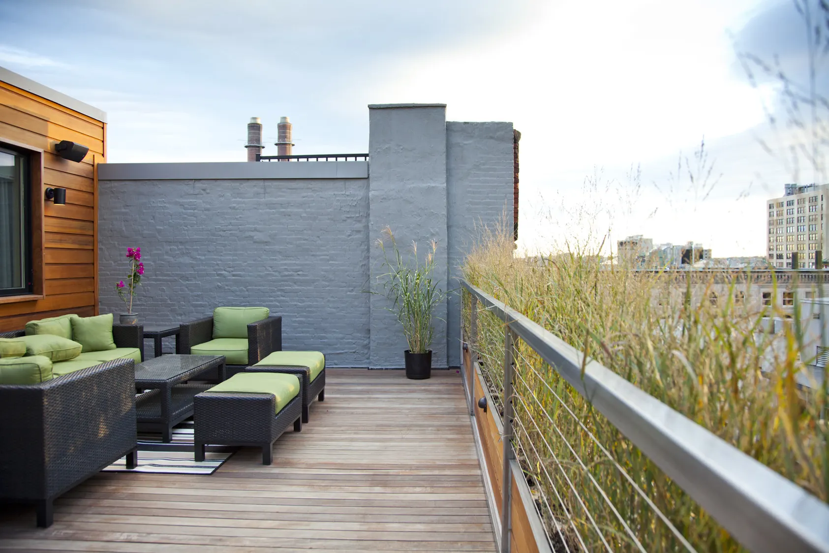 Outdoor sofas with green cushions on the deck, with grasses planted along the rail.