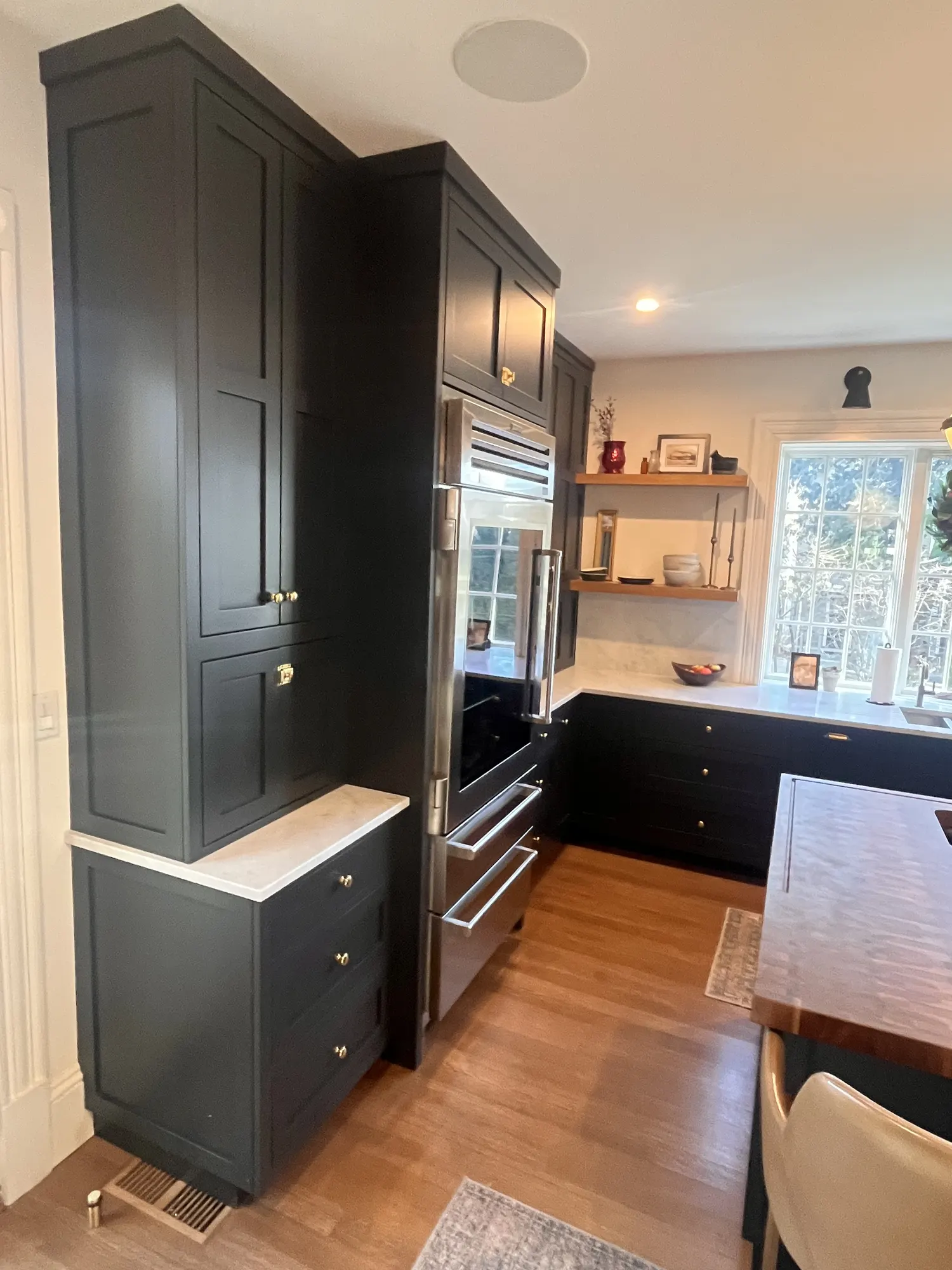 Floor-to-ceiling dark cabinets and a column of built-in ovens, the window wall beyond.