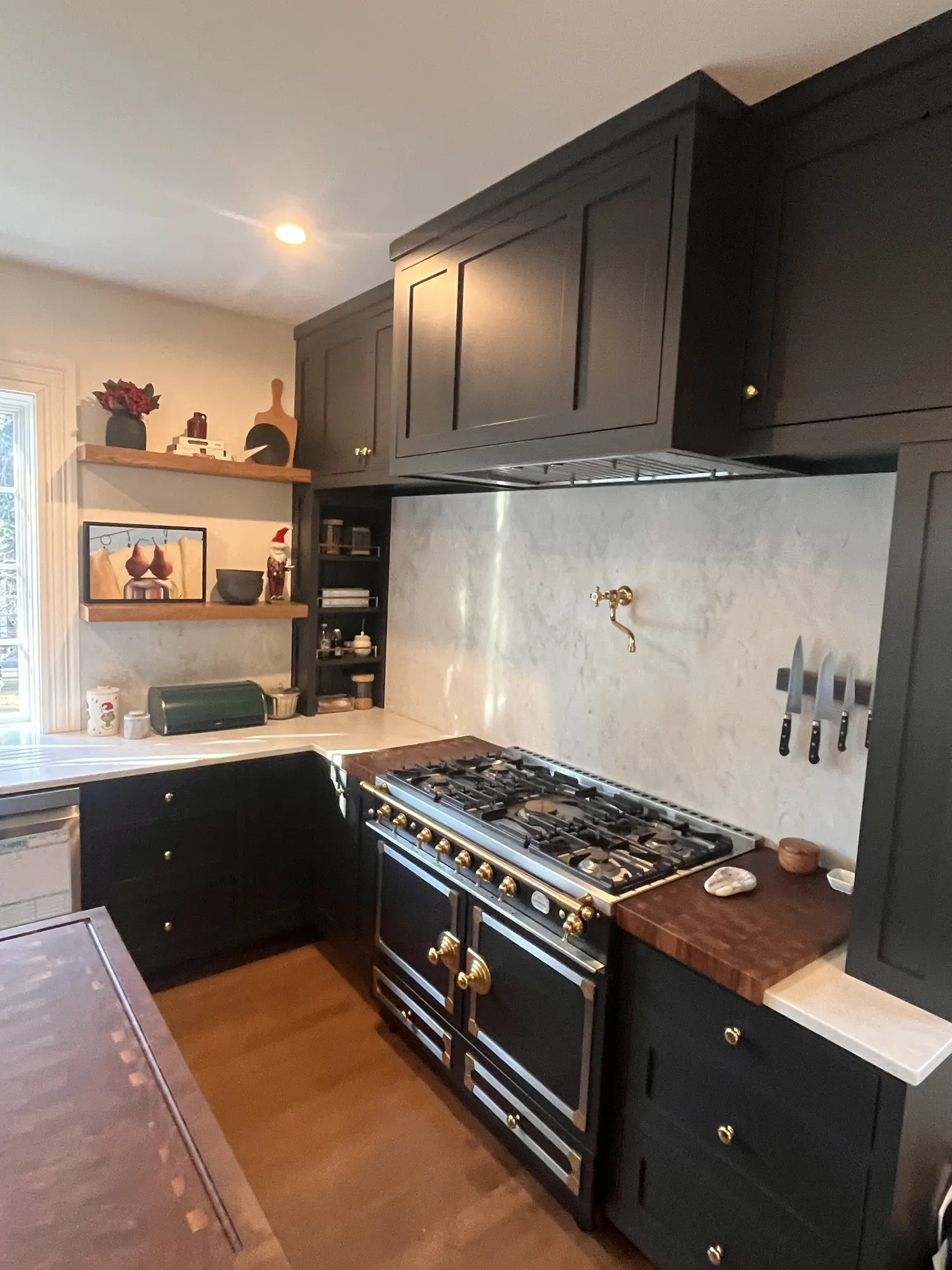 The range under a dark cabinet hood, between marble counters, with the end of the walnut island in front.