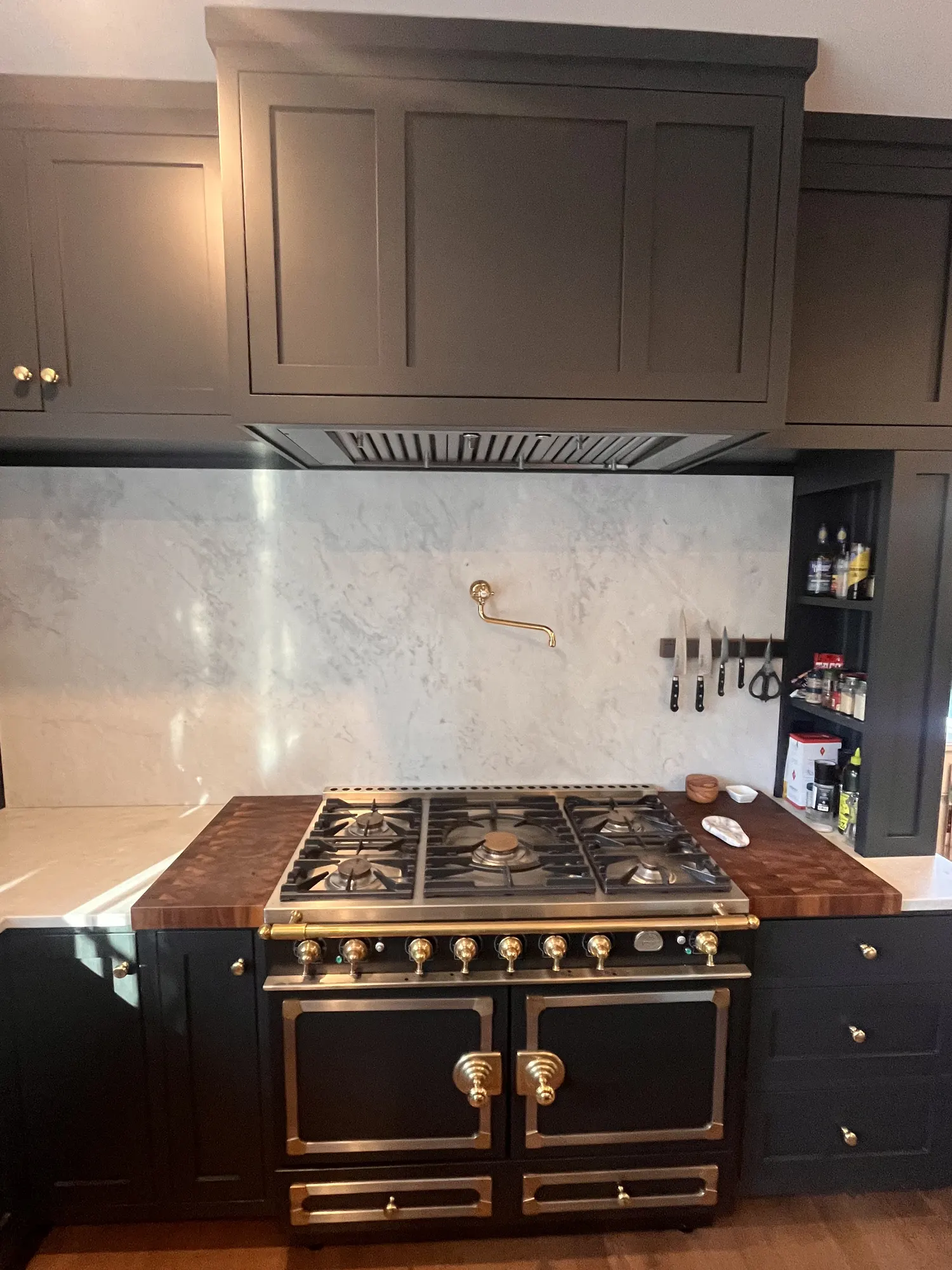 A black and brass range under a panelled hood, with marble behind it and a knife rail beside.