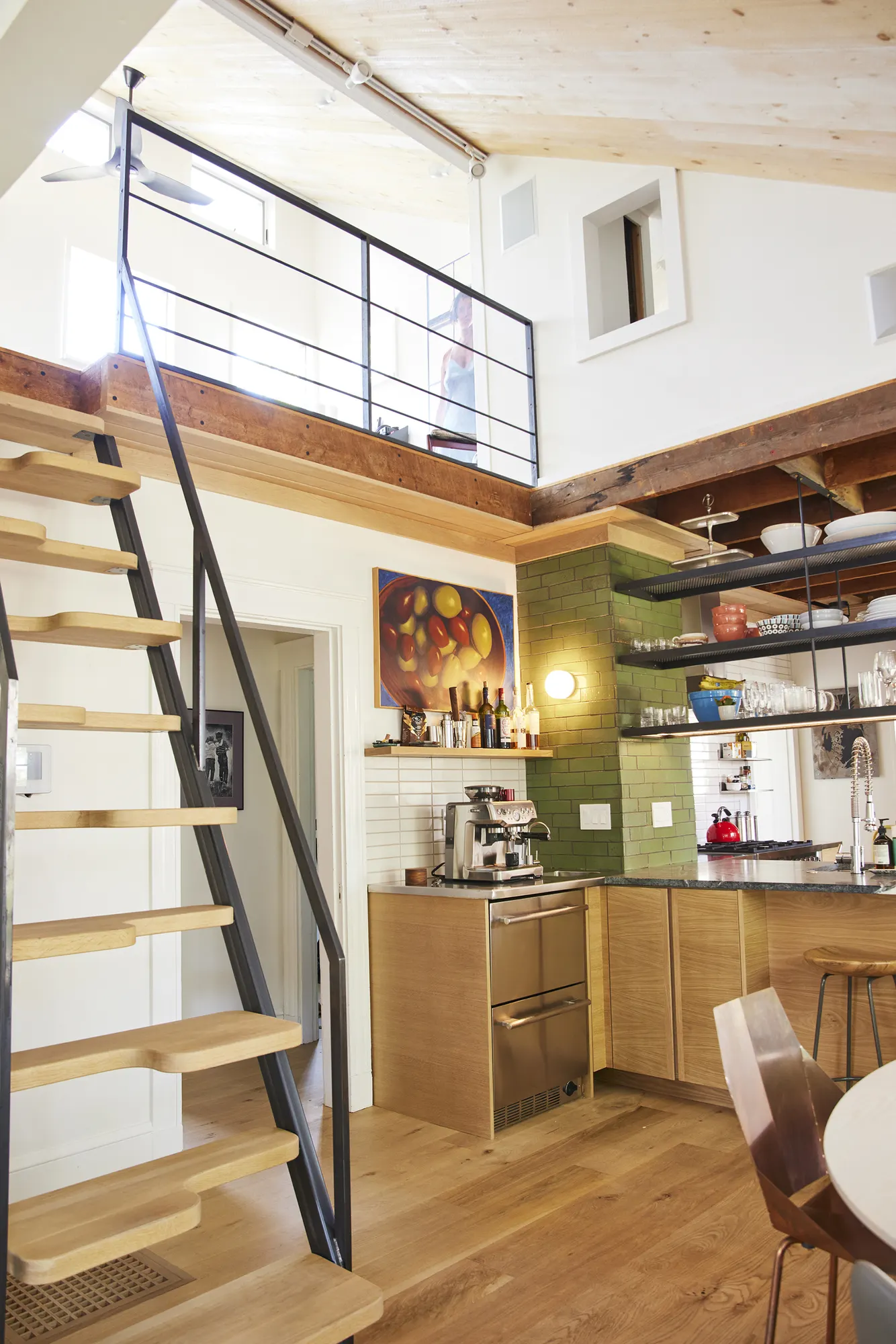 A steep open-tread stair rising past the kitchen to a railed loft.