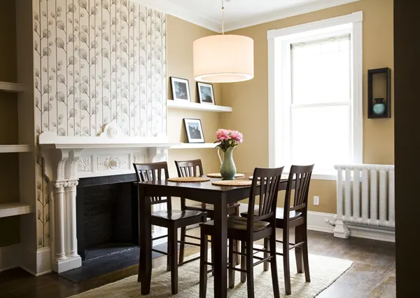 Washington Street Contemporary: a dining table by a white carved fireplace under a drum pendant, with patterned wallpaper on the chimney breast