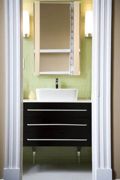 A glass shower in green subway tile, beside the black vanity.